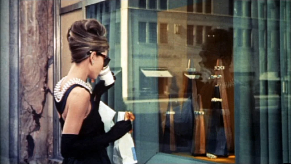 Audrey Hepburn as Holly Golightly, wearing sunglasses and gloves outside a shop in a Breakfast at Tiffany’s trailer frame
